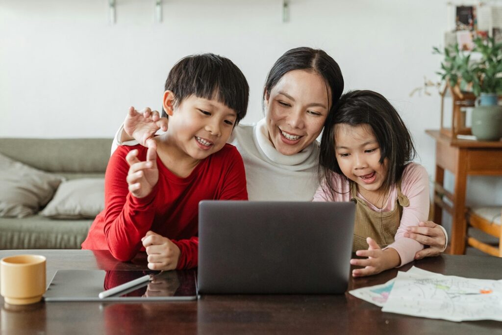 miling Asian mother with her two children, all looking at a laptop screen. ICGC, London POWER TEMPLE