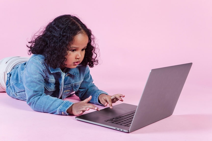A young black girl lying on the floor with her laptop, engrossed in her work on laptop, pink background, at icgc canning town